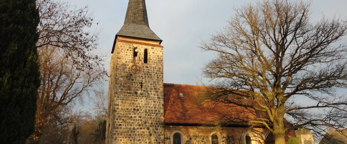 A stone church with a tall steeple and a brick building with arched windows.