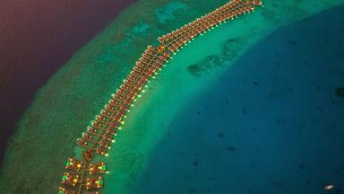 Aerial view of bungalows along the reef at sunset on Baa Atoll, Kanifushi Island, Maldives.