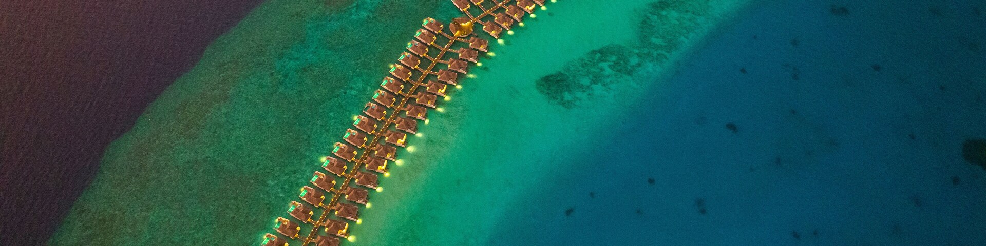 Aerial view of bungalows along the reef at sunset on Baa Atoll, Kanifushi Island, Maldives.