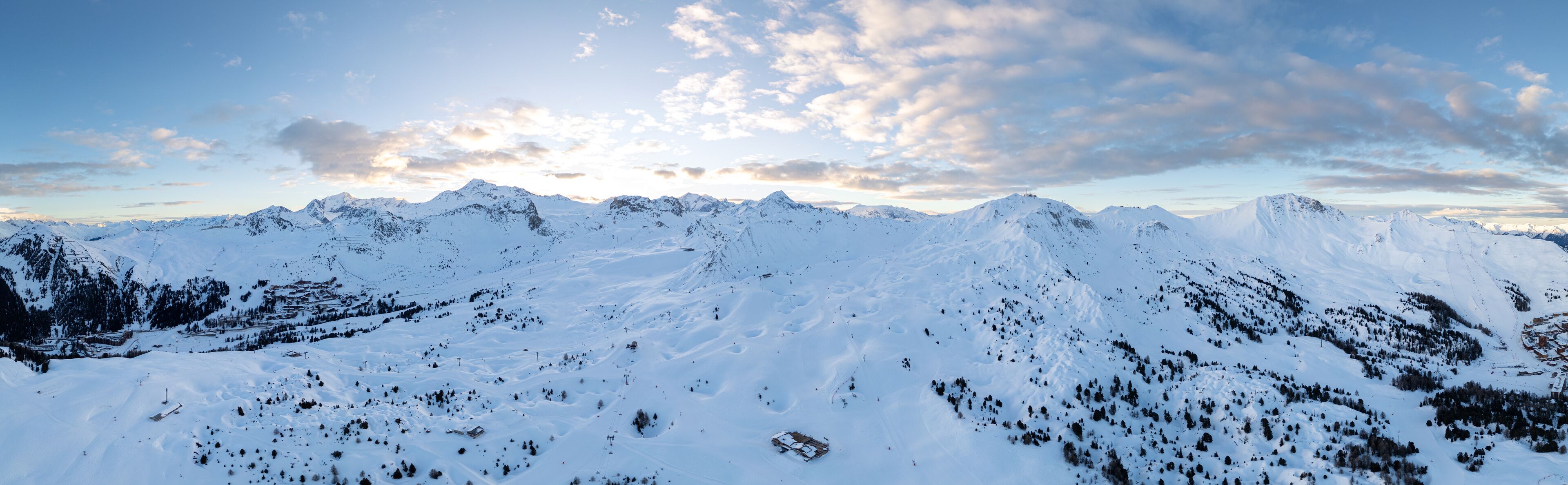 A snow-covered mountain range with clear skies and scattered clouds.