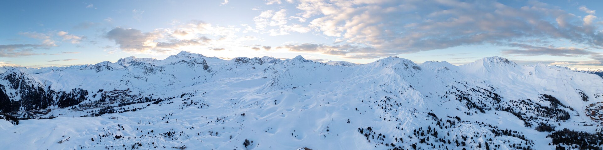 A snow-covered mountain range with clear skies and scattered clouds.