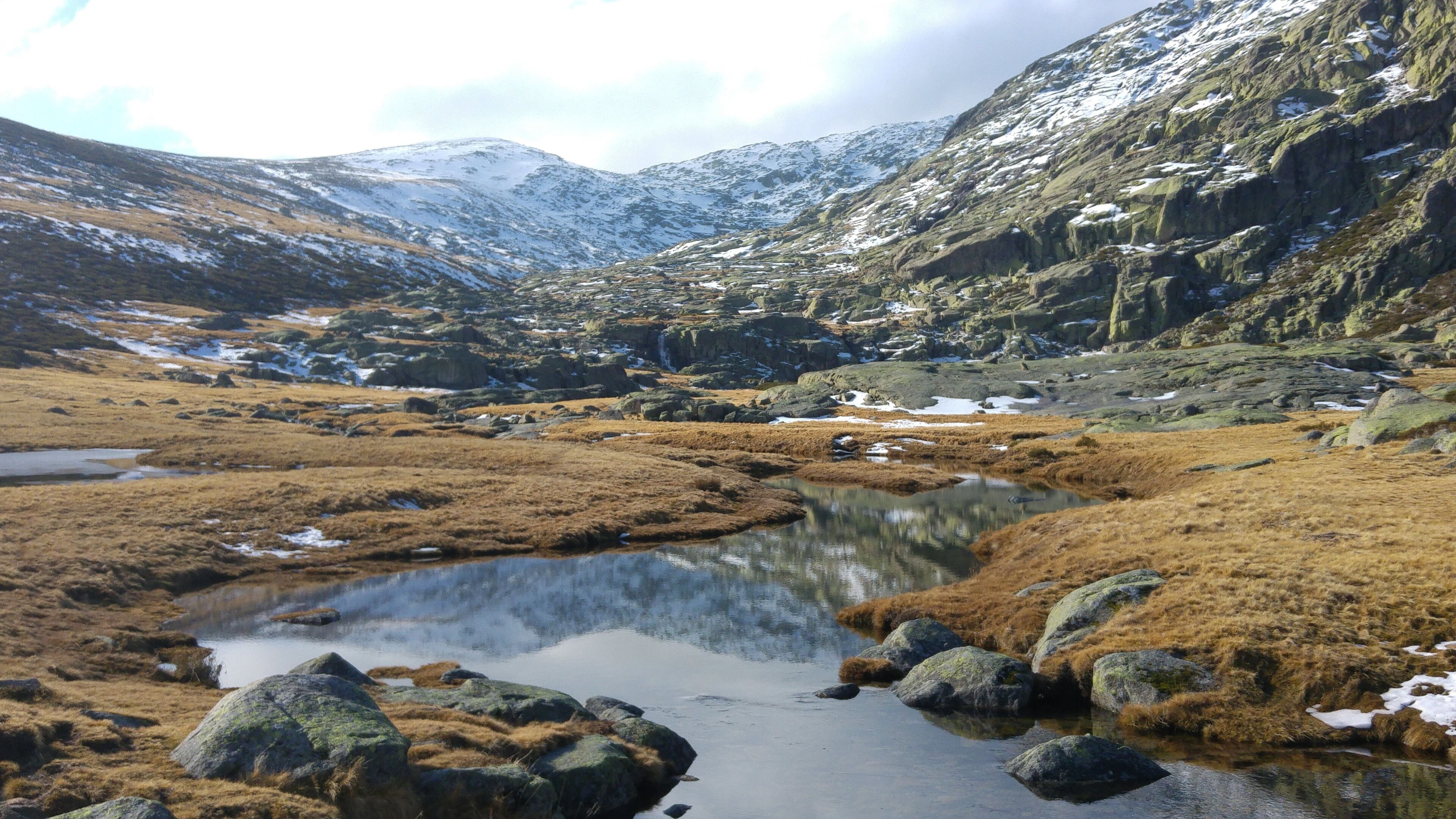 A mountainous landscape with a small lake surrounded by rocky terrain and patches of snow.