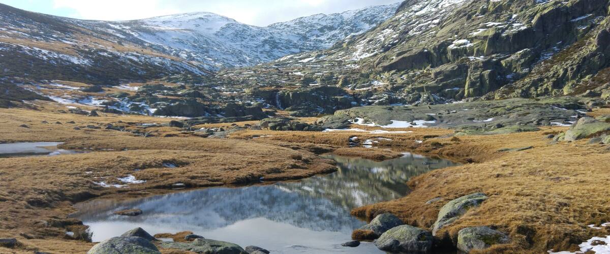 A mountainous landscape with a small lake surrounded by rocky terrain and patches of snow.