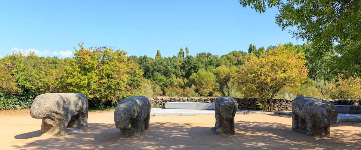 Three stone elephant sculptures in a park with trees and a stone wall in the background.
