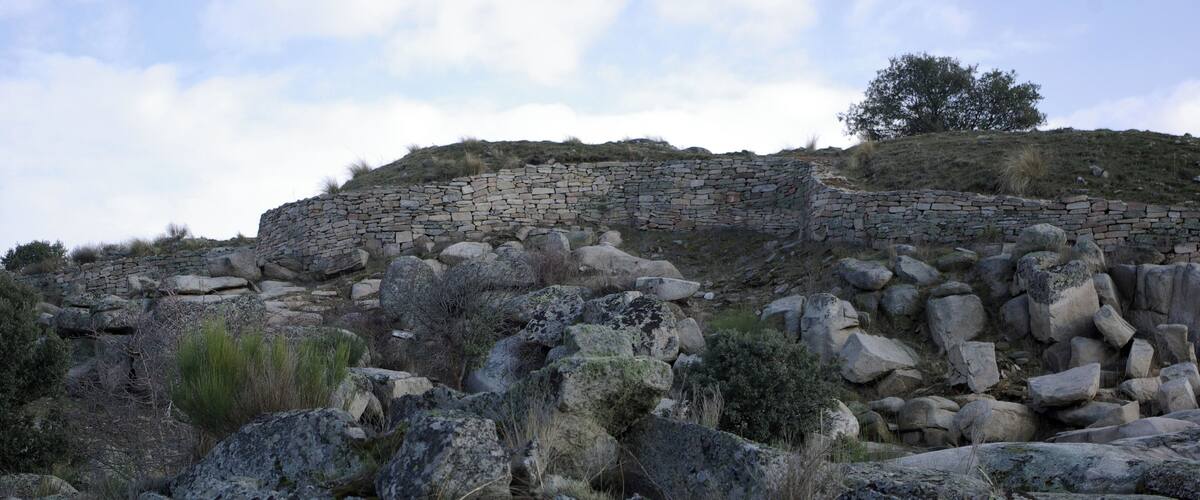 A stone wall on a hillside with scattered rocks and sparse vegetation.