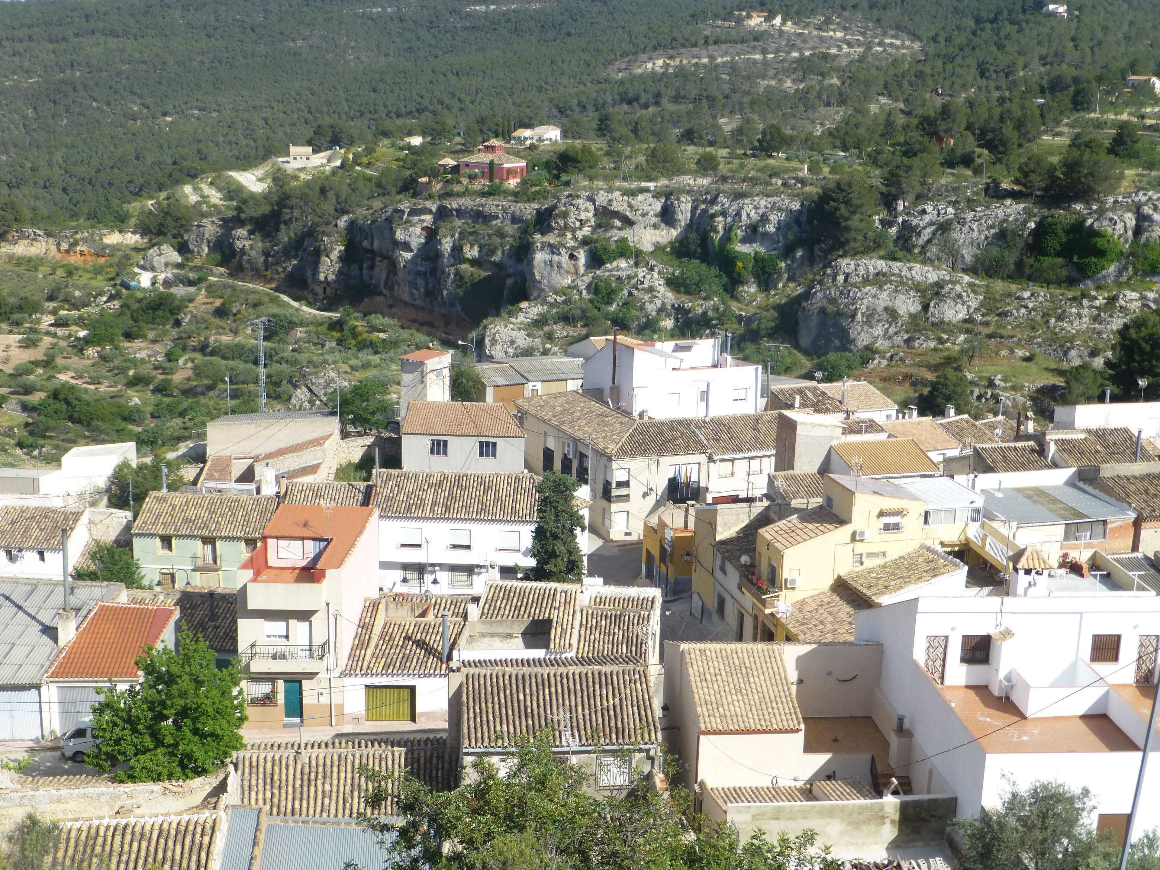 A coastal village with terracotta-roofed buildings, a rocky hillside, and a clear view of the sea.
