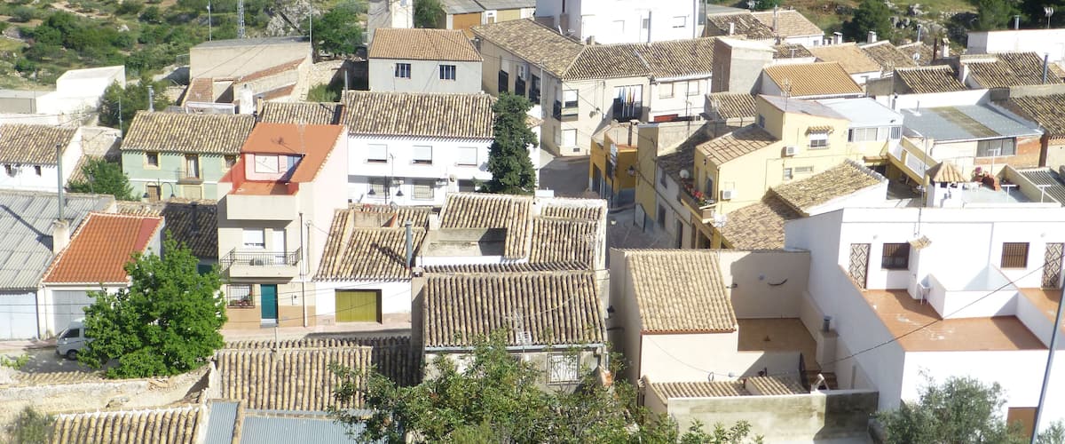 A coastal village with terracotta-roofed buildings, a rocky hillside, and a clear view of the sea.