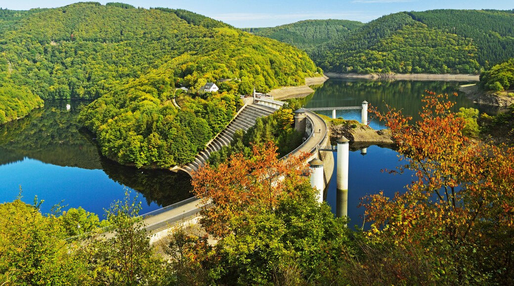 A dam with a bridge, surrounded by lush green hills and a calm lake.