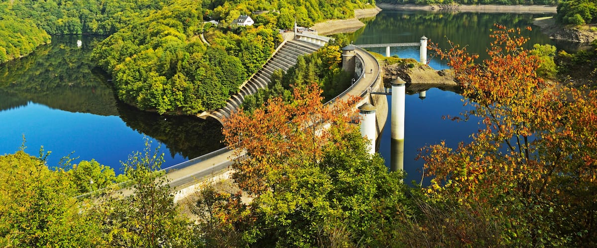 A dam with a bridge, surrounded by lush green hills and a calm lake.