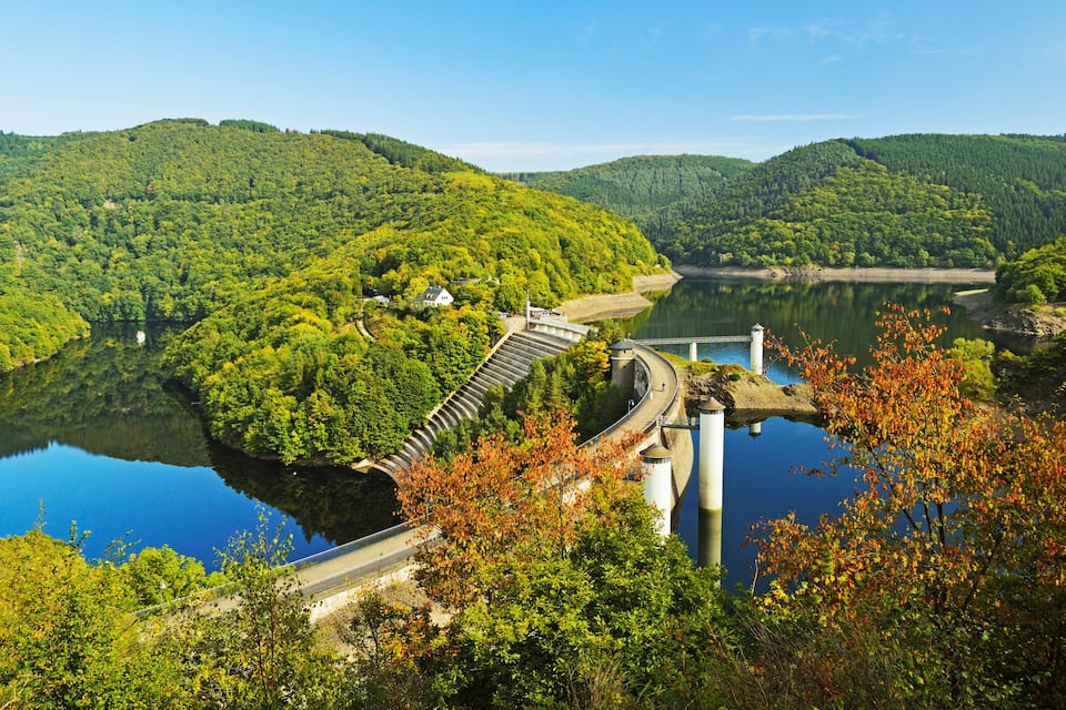 A dam with a bridge, surrounded by lush green hills and a calm lake.