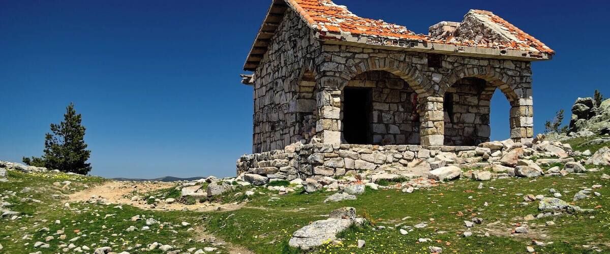 A stone structure with a tiled roof and arched openings, surrounded by a grassy landscape with scattered rocks.