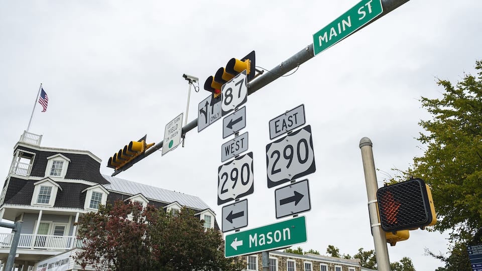 Street signs for Route 87, Route 290, and Main St, with a traffic light and a house in the background.