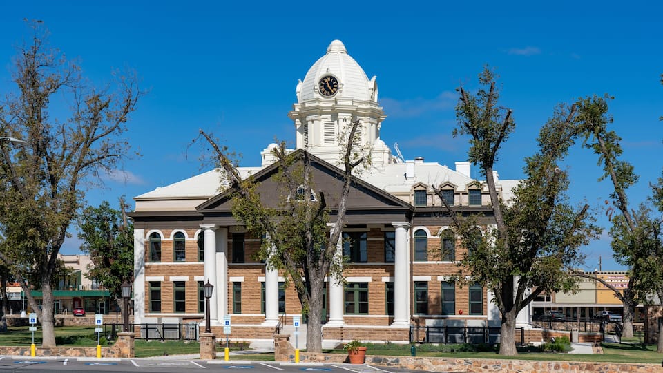 A large white building with a clock tower, surrounded by trees and a clear blue sky.