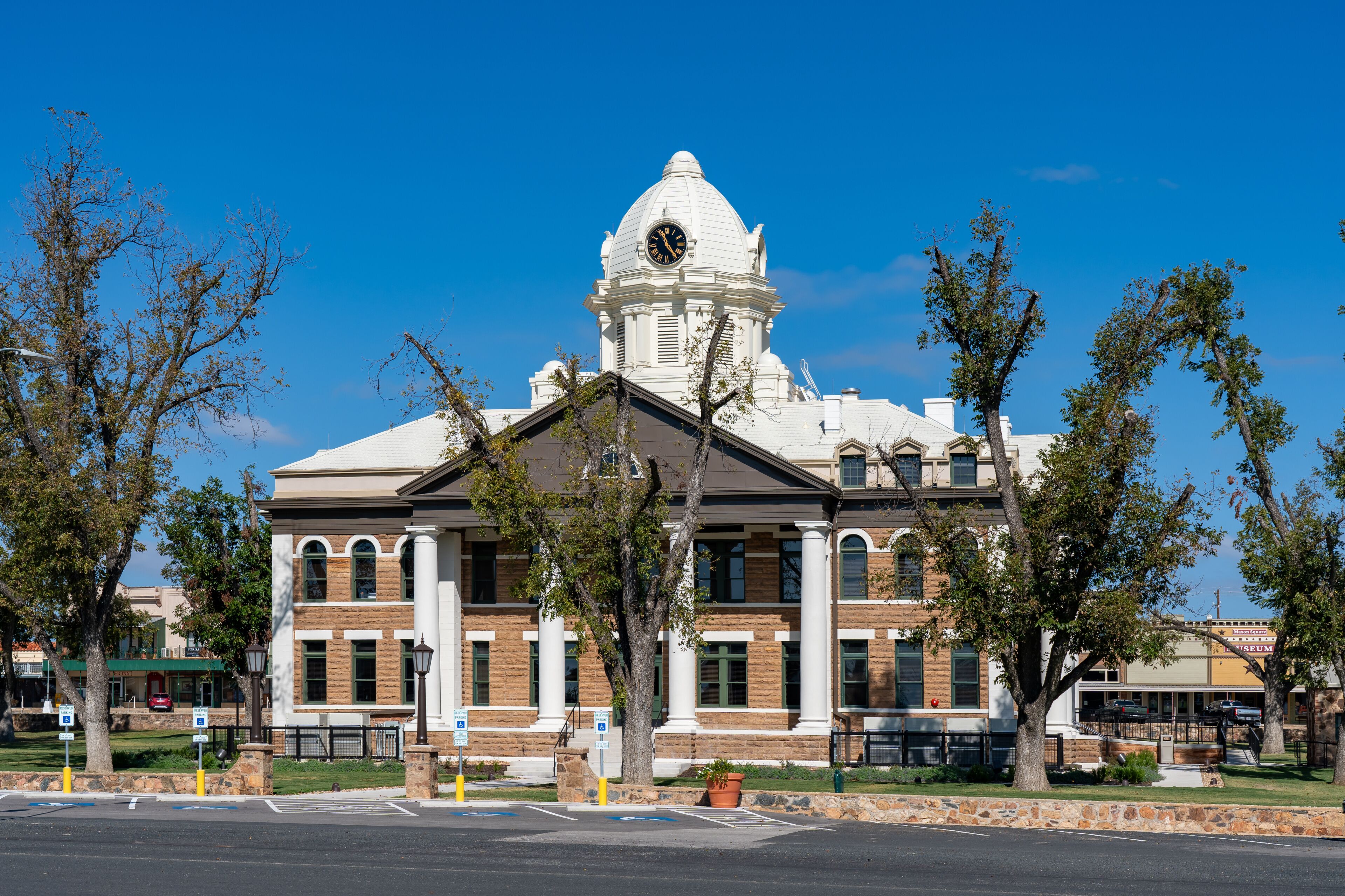 A large white building with a clock tower, surrounded by trees and a clear blue sky.