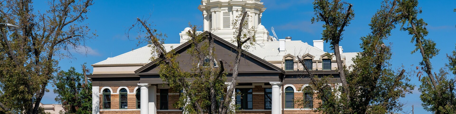 A large white building with a clock tower, surrounded by trees and a clear blue sky.