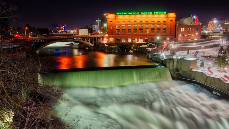 A night view of a dam with a waterfall, a bridge, and the Washington Water Power building.