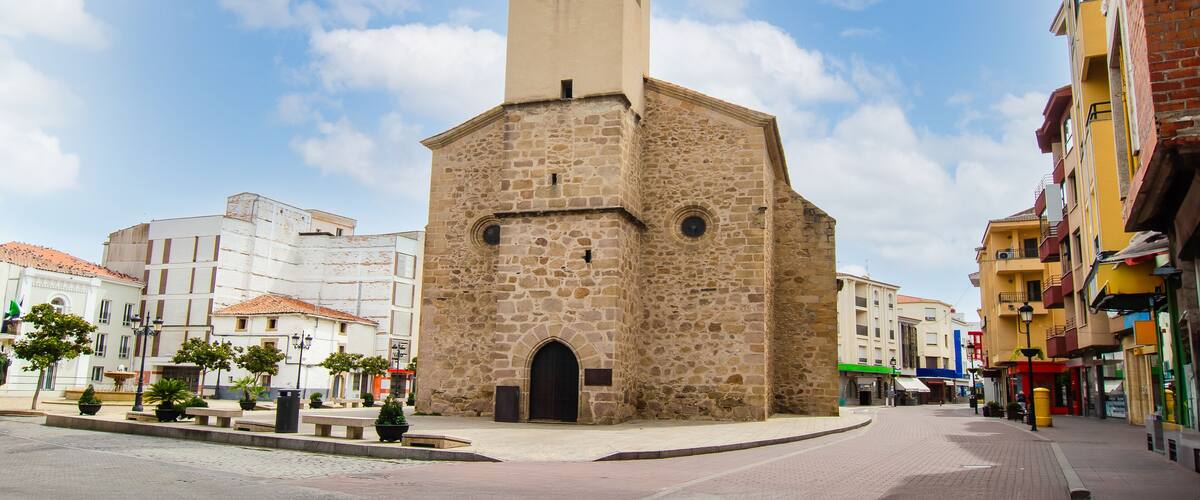 A historic stone church with a bell tower, surrounded by a cobblestone square and colorful buildings.