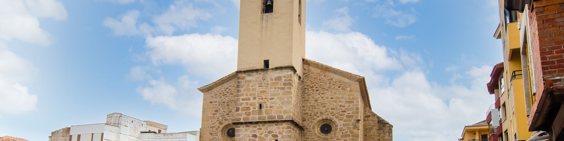 A historic stone church with a bell tower, surrounded by a cobblestone square and colorful buildings.