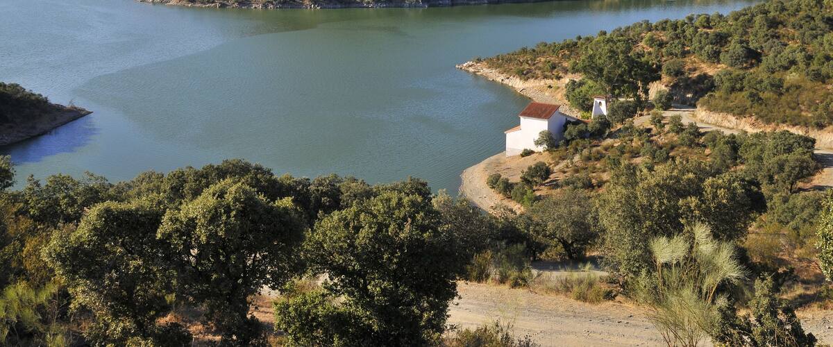 A lake surrounded by hills with sparse vegetation and a few buildings near the shore.
