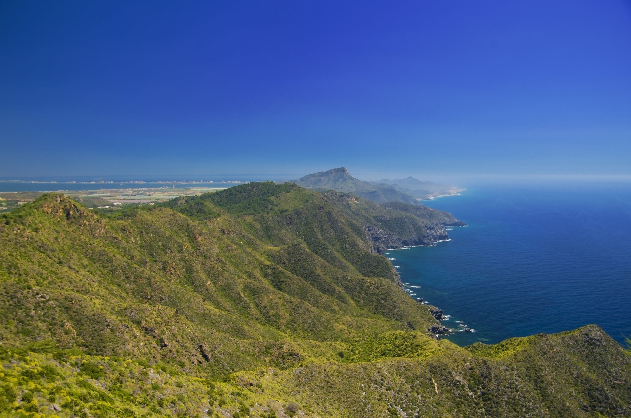 A coastal landscape with green hills and a clear blue sea.