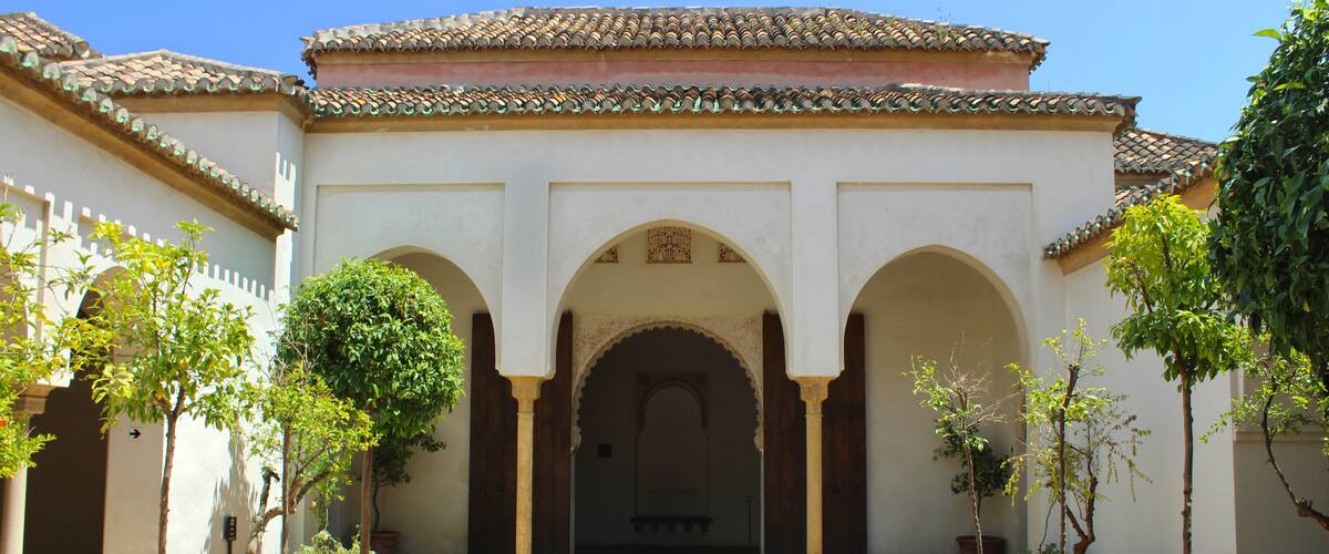 A courtyard with arches, potted plants, and a tiled roof.