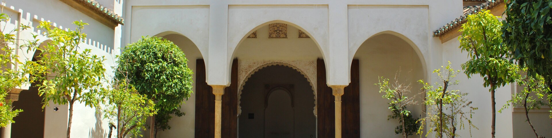 A courtyard with arches, potted plants, and a tiled roof.