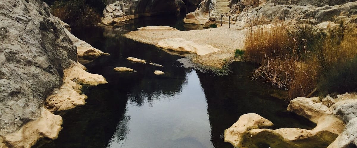 A narrow canyon with a clear water stream, rocky walls, and a staircase leading up.