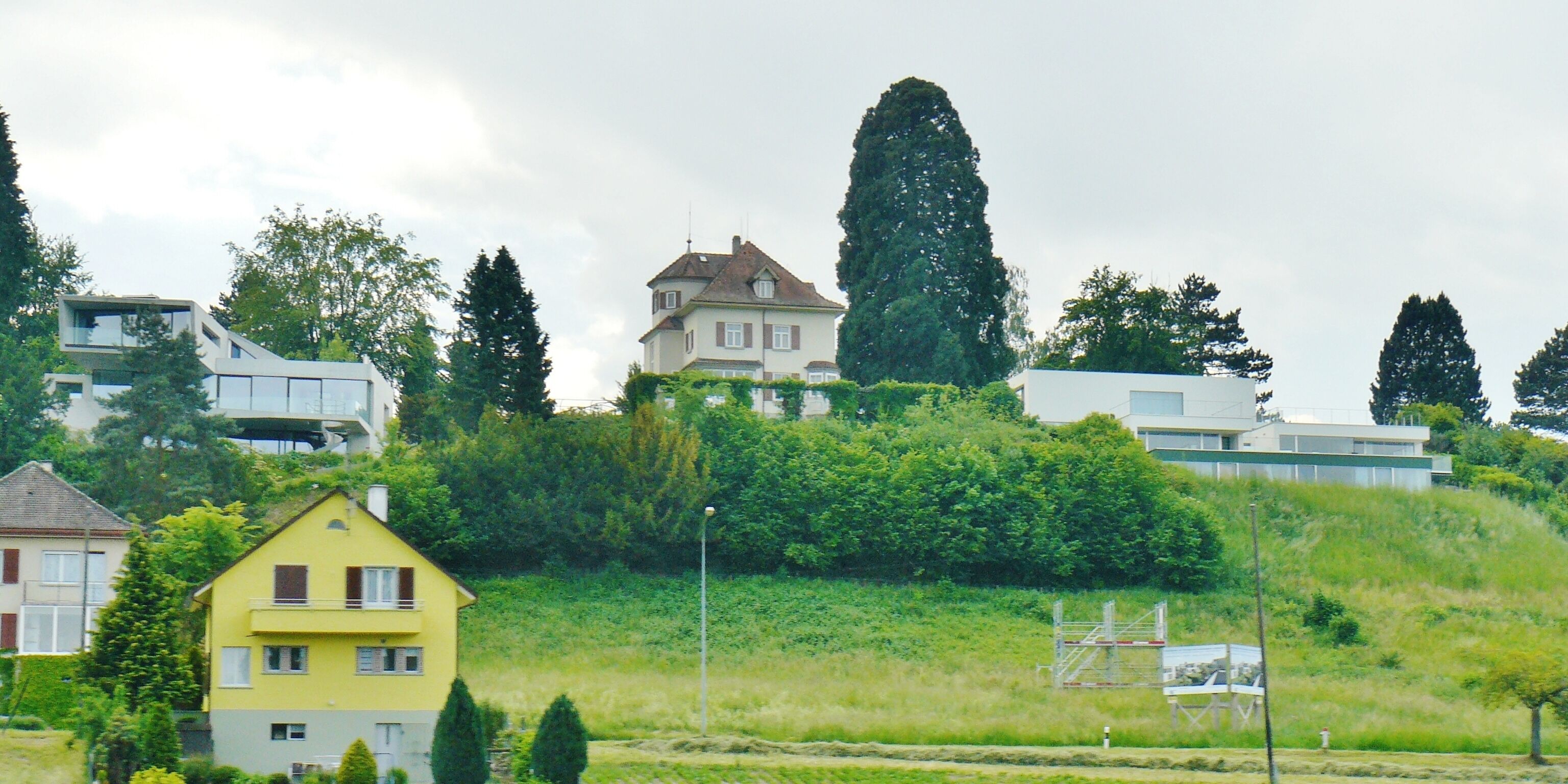 A residential area with houses on a hillside, surrounded by greenery and trees.