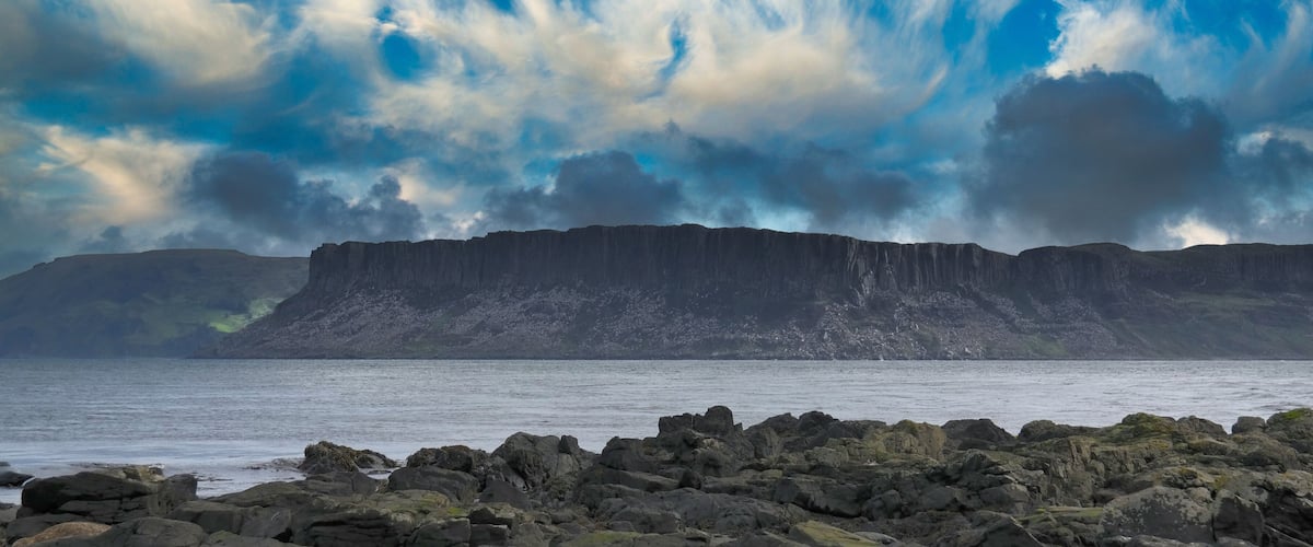 A rugged coastline with large rock formations and a dramatic sky.
