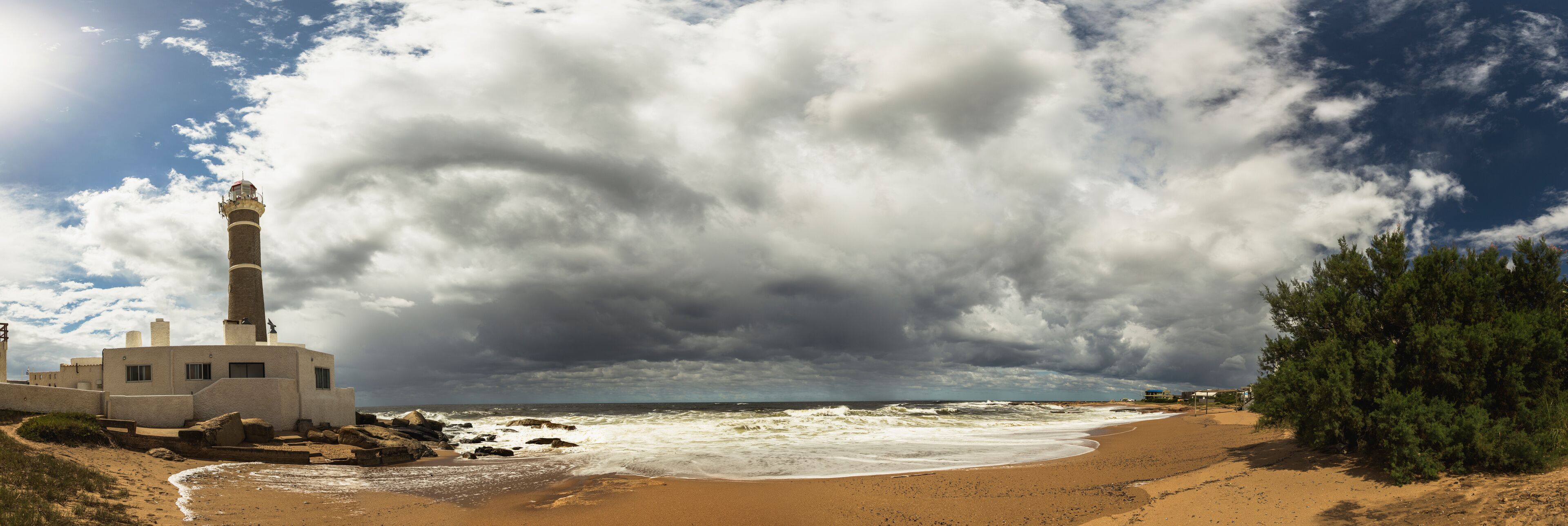 A coastal scene with a lighthouse, beach, rocky shoreline, and stormy sky.