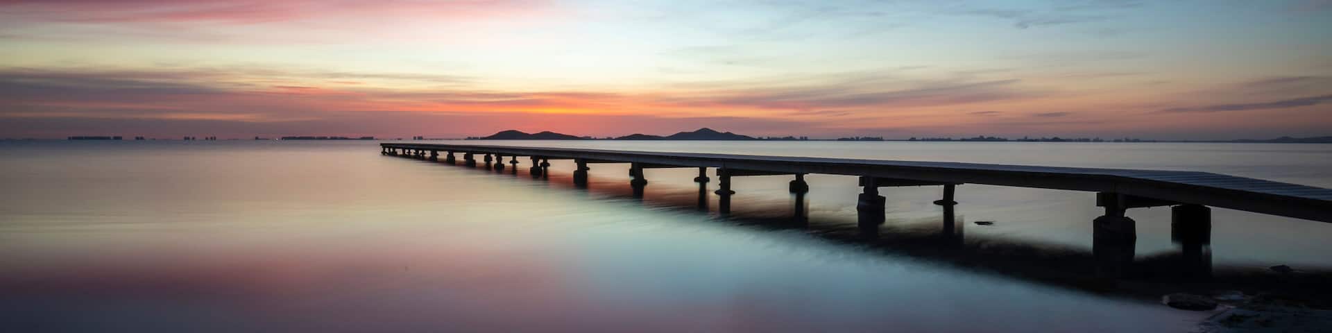 Beautiful wide landscape at sunrise in the Mar Menor, Cartagena, Spain. With a spectacular very colorful sky and reflected in the calm waters of the sea. We also see a wooden jetty on the water. It t