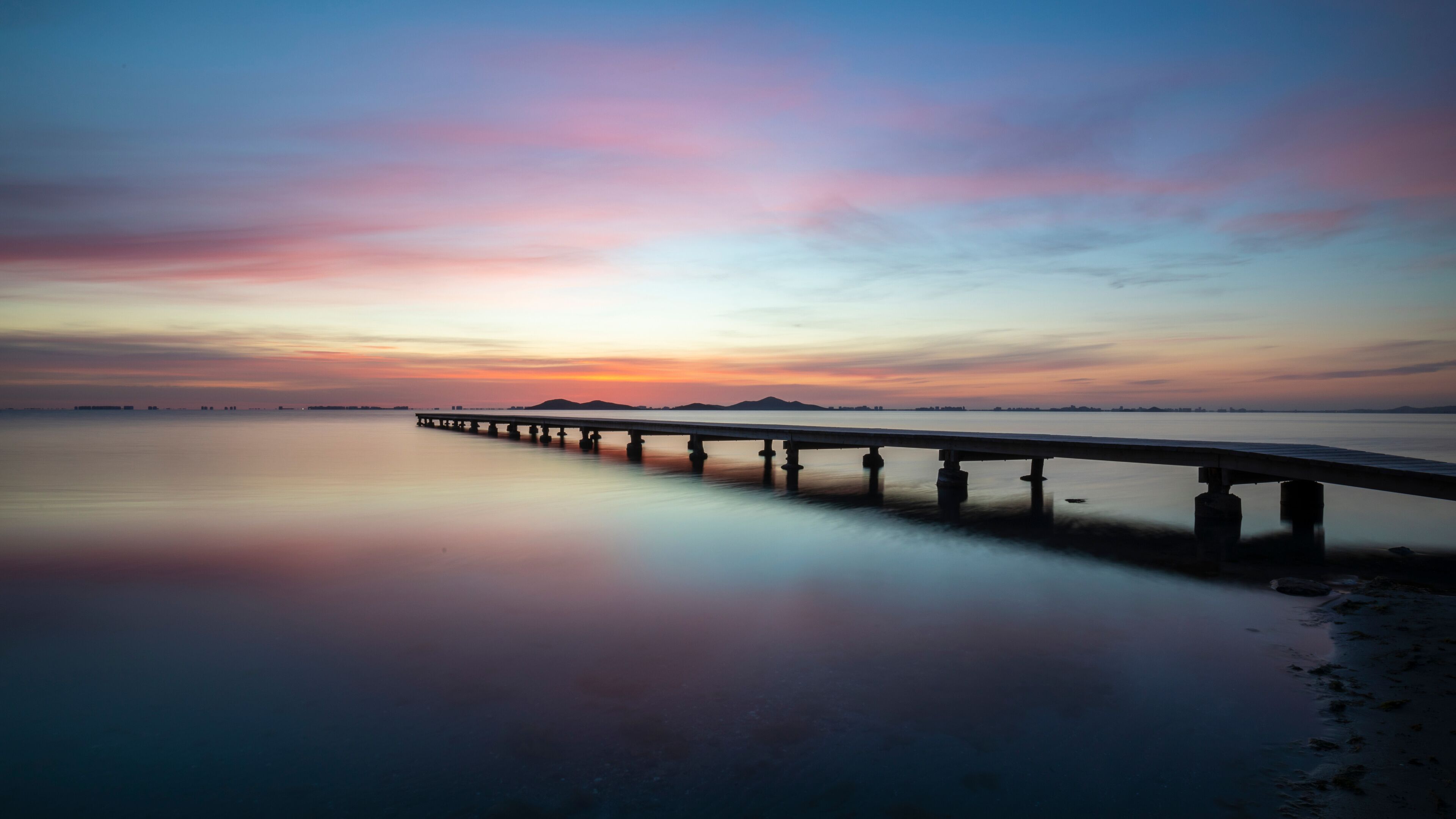 A long pier extending into calm waters at sunset.