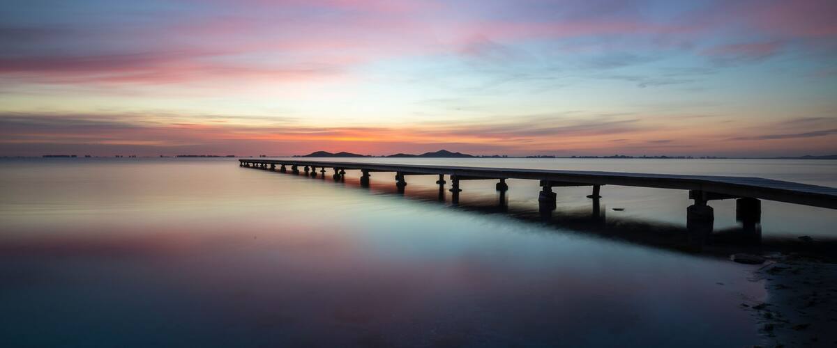 A long pier extending into calm waters at sunset.