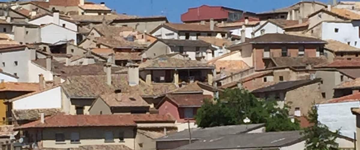 A narrow dirt path flanked by houses with red roofs, leading uphill in a hilly residential area.