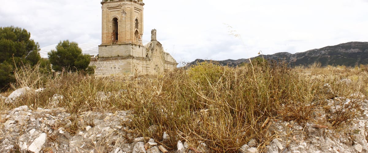 An old stone bell tower surrounded by dry grass and rocks.