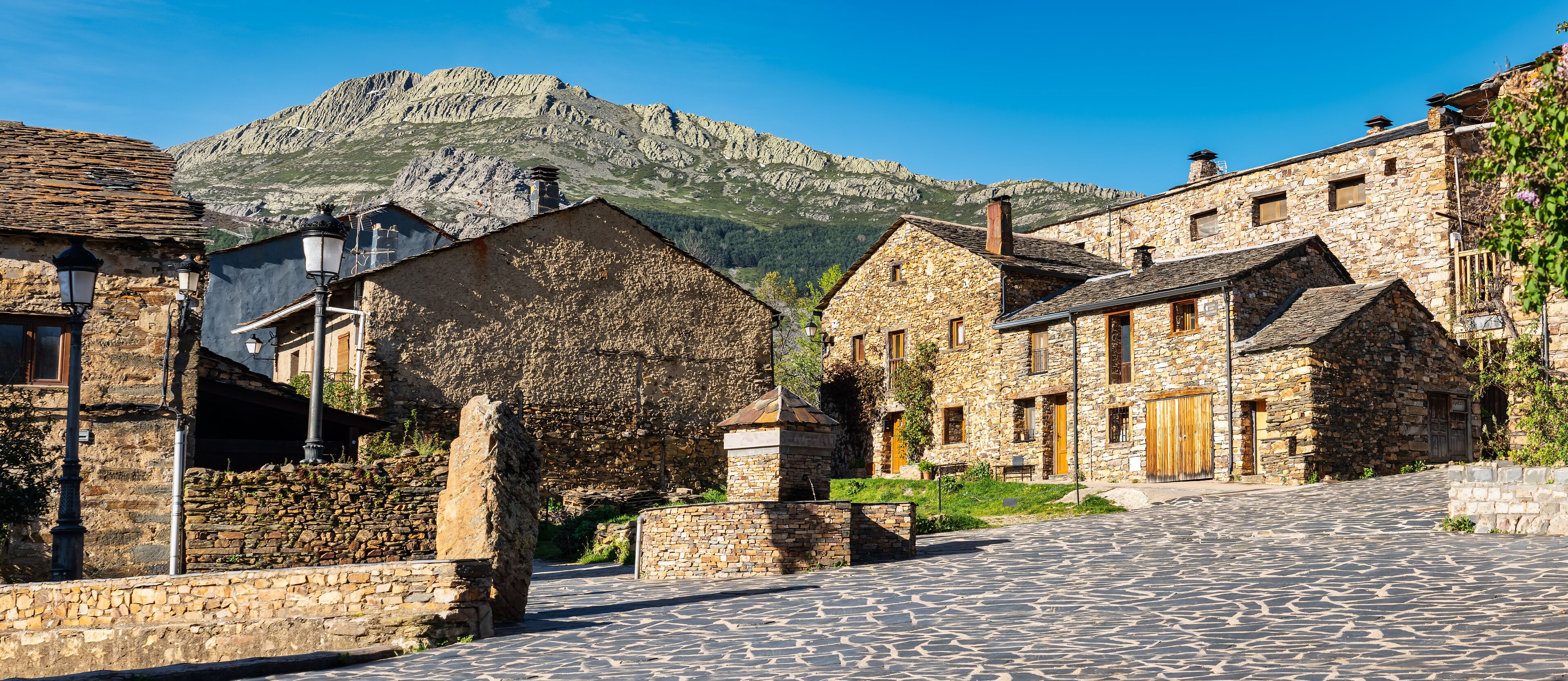 A cobblestone street in a historic village with stone buildings and a mountain in the background.