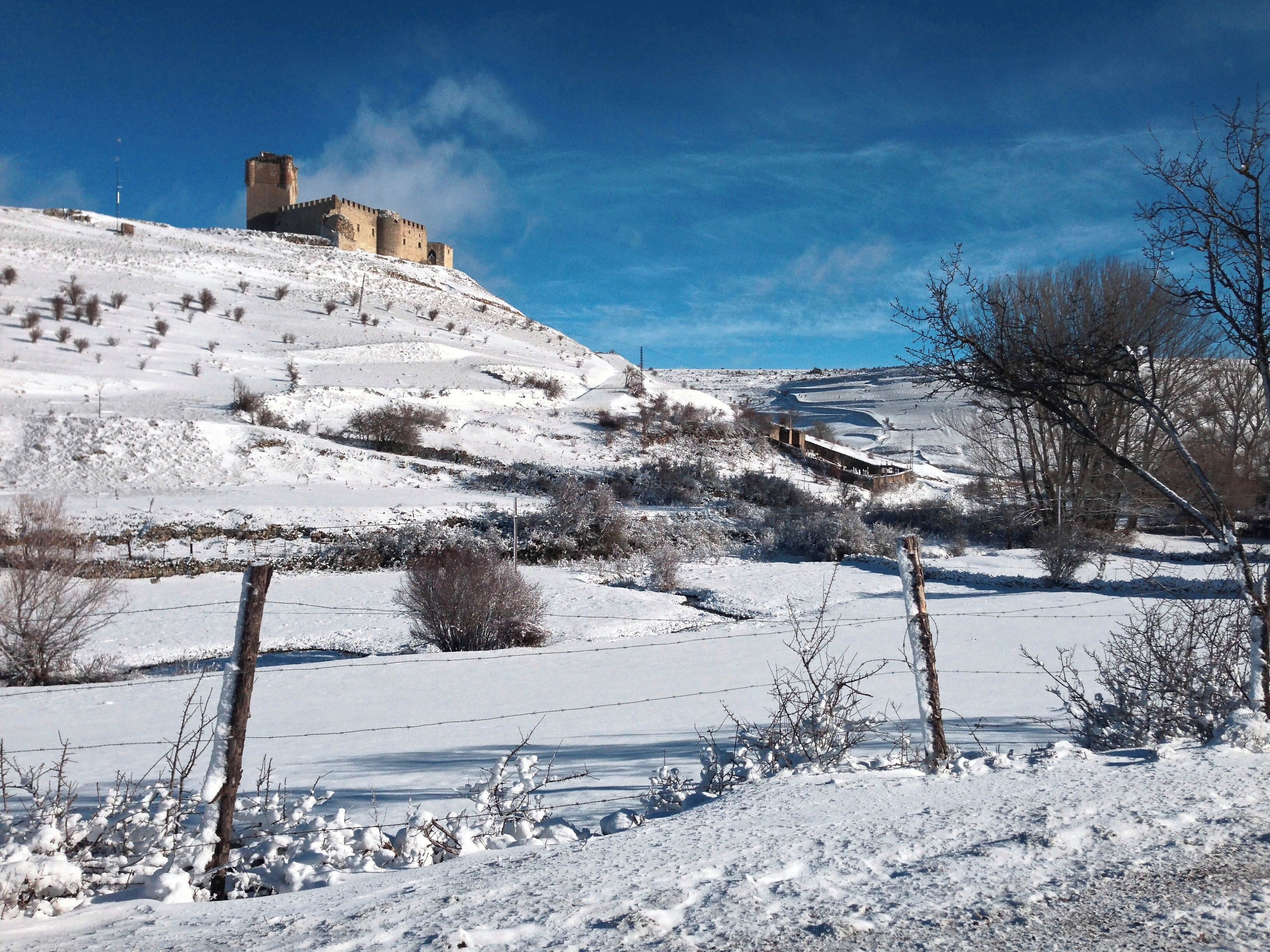 A snow-covered landscape with a castle on a hill and a clear blue sky.