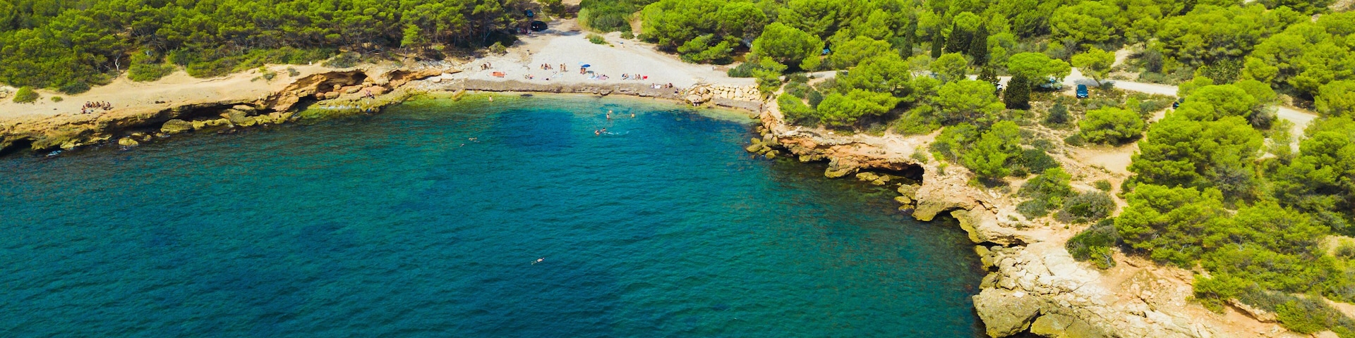 A coastal landscape with a beach, clear blue waters, and dense green vegetation.