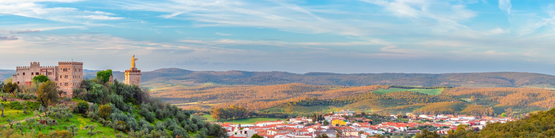 A historic castle, a statue, and a town nestled in a valley.