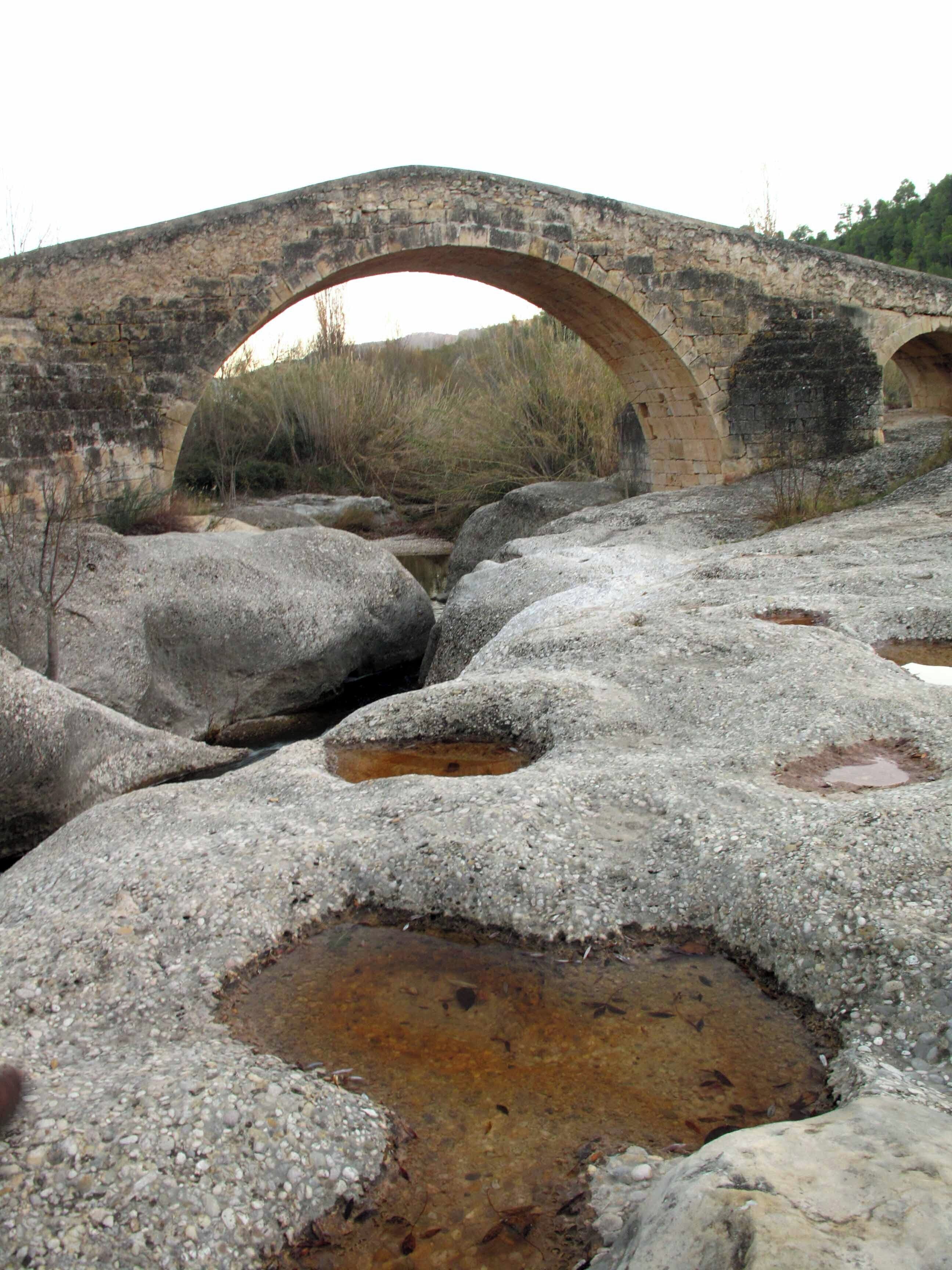 A stone bridge arching over a rocky stream with visible water erosion.
