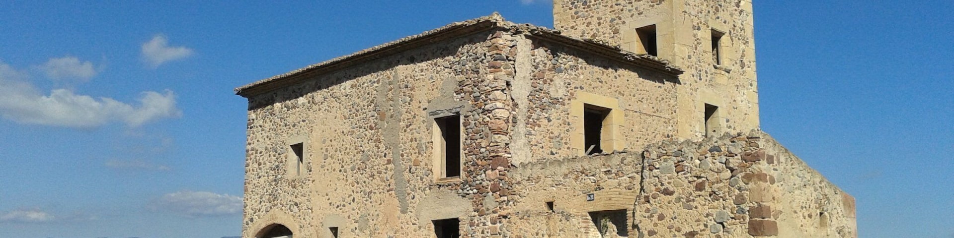 An old stone building with a tower, surrounded by grass and mountains in the background.
