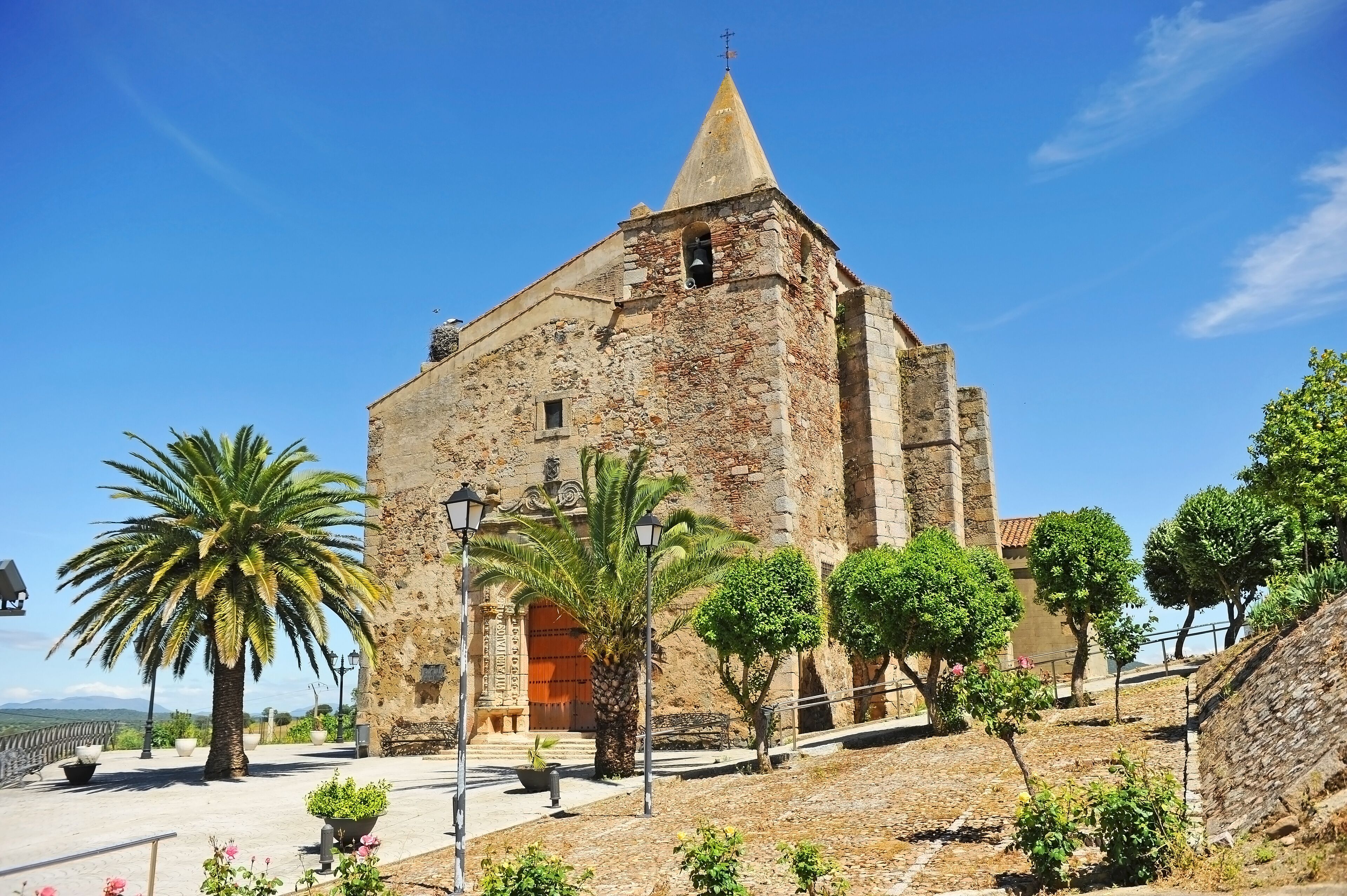 A historic stone building with a conical roof, palm trees, and a clear blue sky.