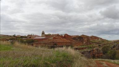 A rural village with traditional stone buildings, a church, and rolling hills.