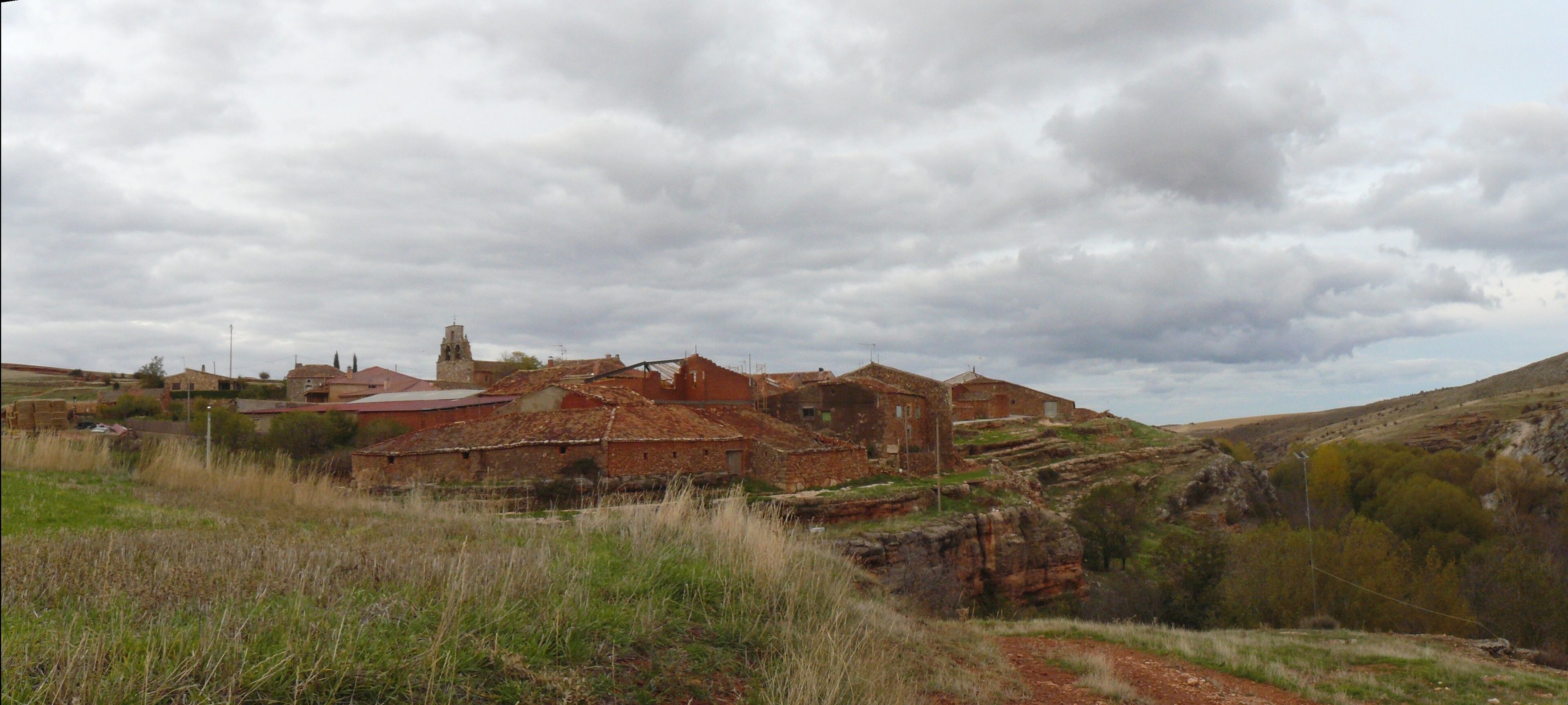 A rural village with traditional stone buildings, a church, and rolling hills.