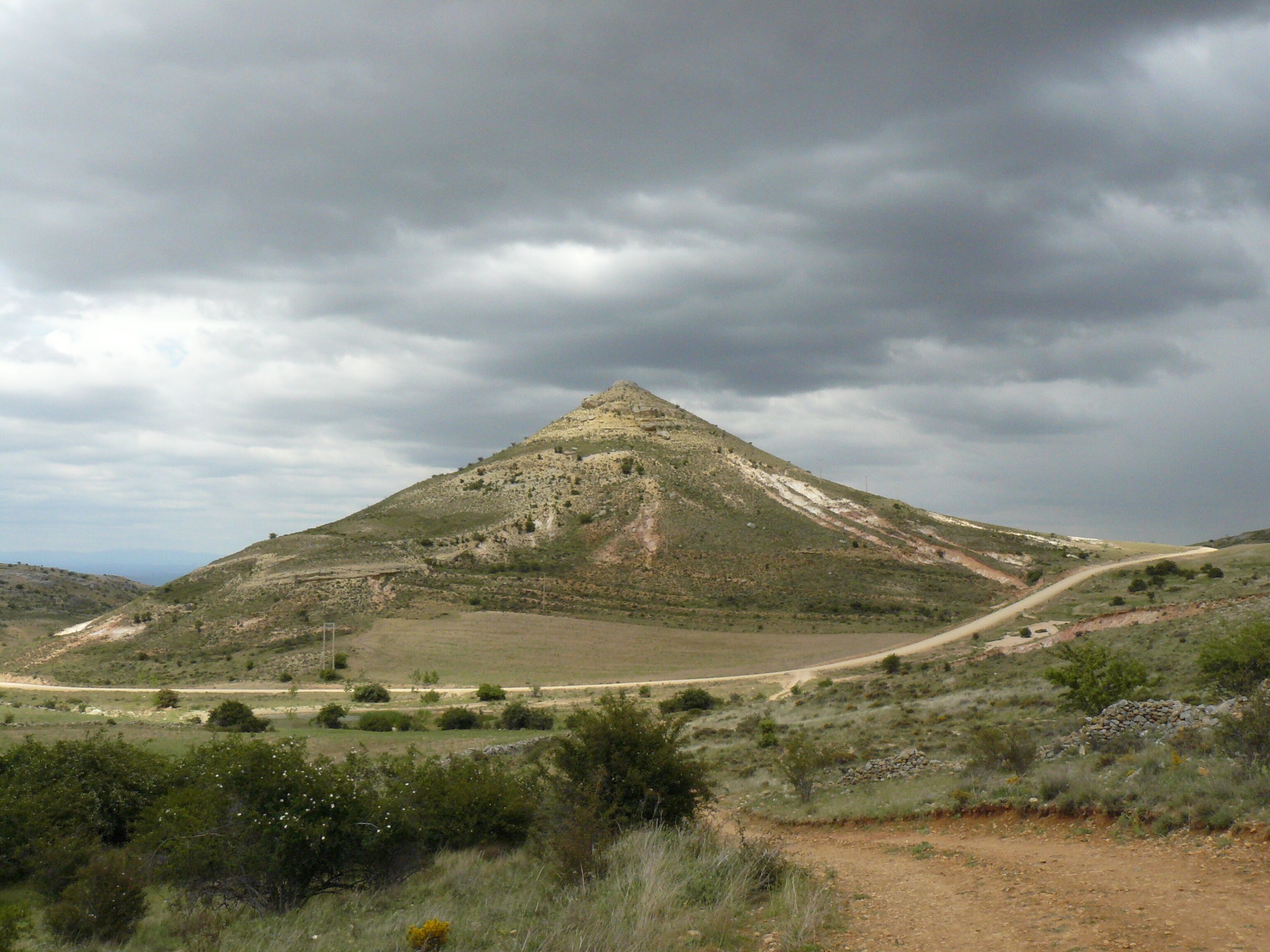A rugged hill with a dirt path leading up to a rocky summit.