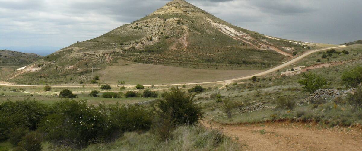 A rugged hill with a dirt path leading up to a rocky summit.