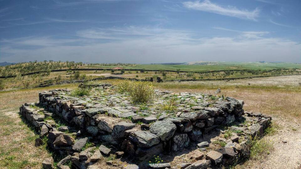 A stone structure in a grassy field with a clear sky and distant hills.