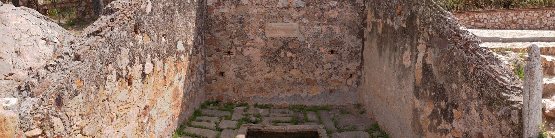 Uma estrutura de pedra antiga com uma pequena piscina e um muro de pedra.