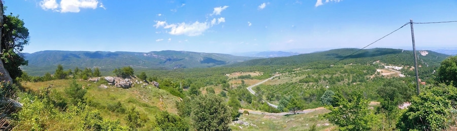 Un paysage montagneux avec une route sinueuse, de vastes forêts et des collines qui s’étendent à l’horizon.
