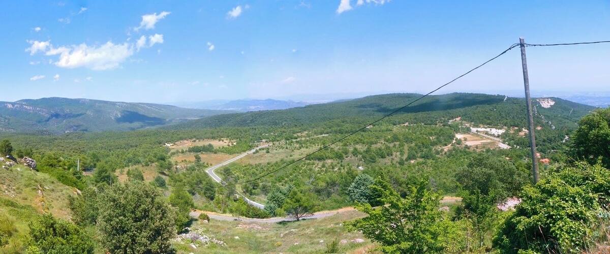 A mountainous landscape with a winding road, dense forests, and distant hills.